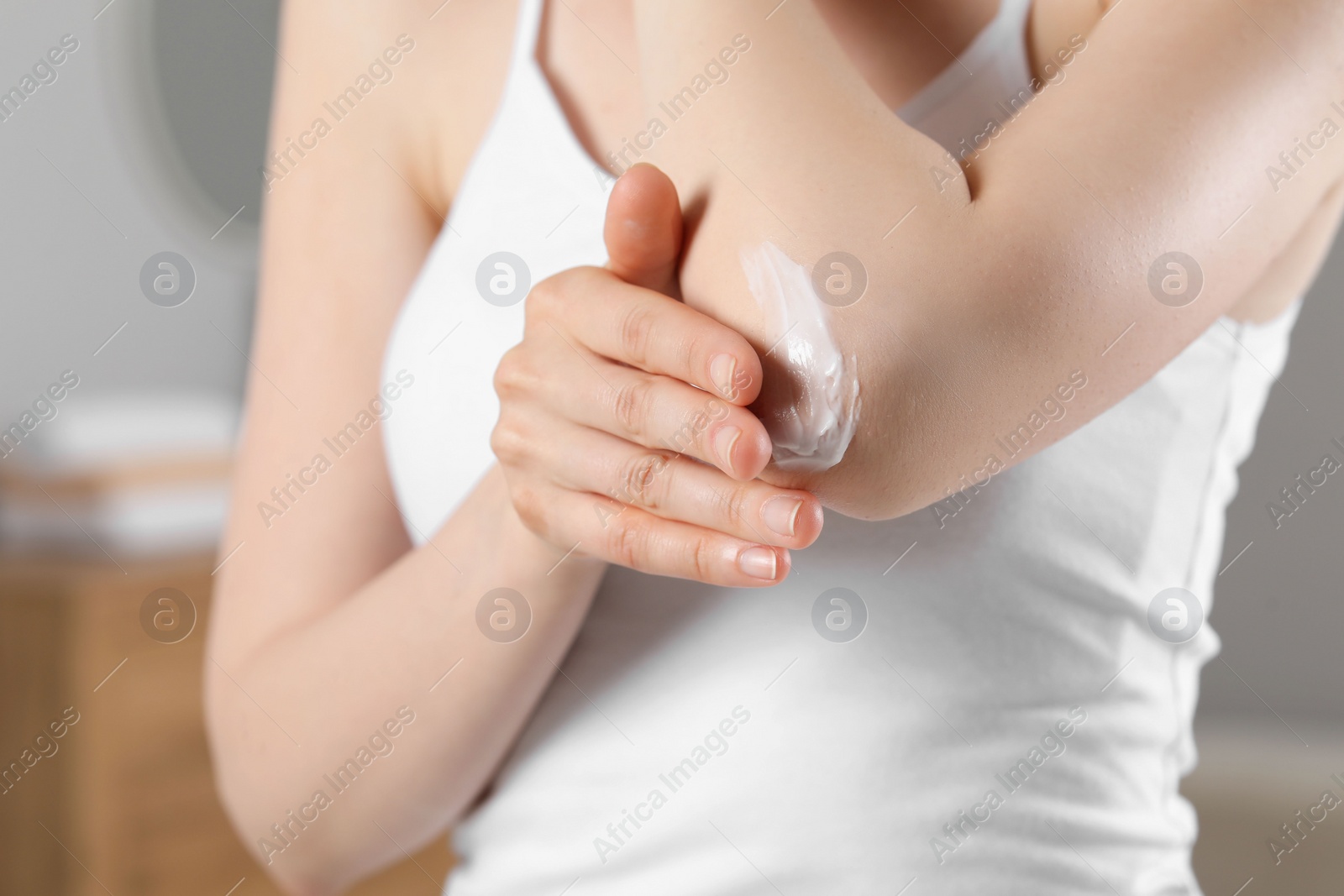 Photo of Woman applying body cream onto elbow indoors, closeup