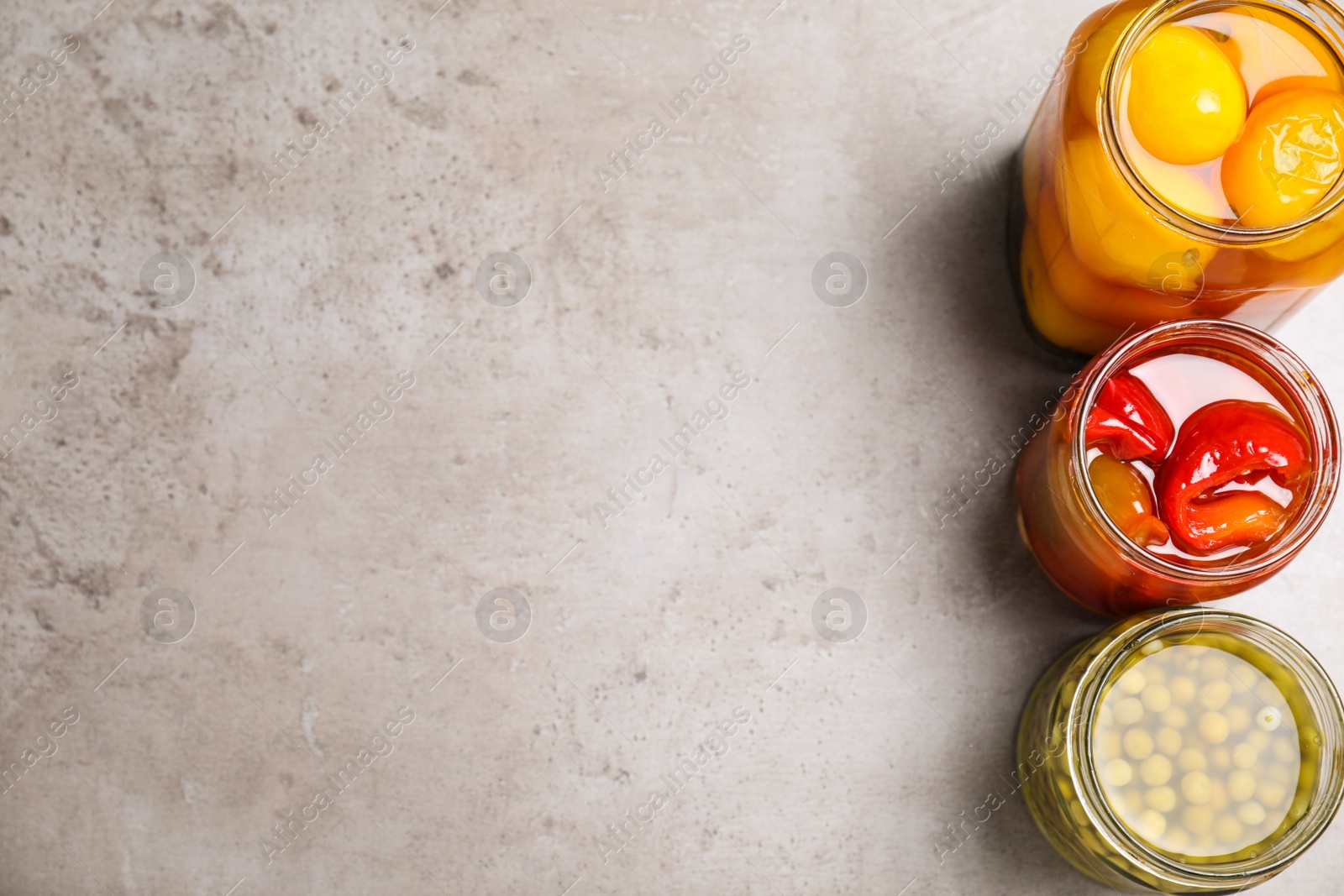 Photo of Glass jars with different pickled vegetables on grey table, flat lay. Space for text