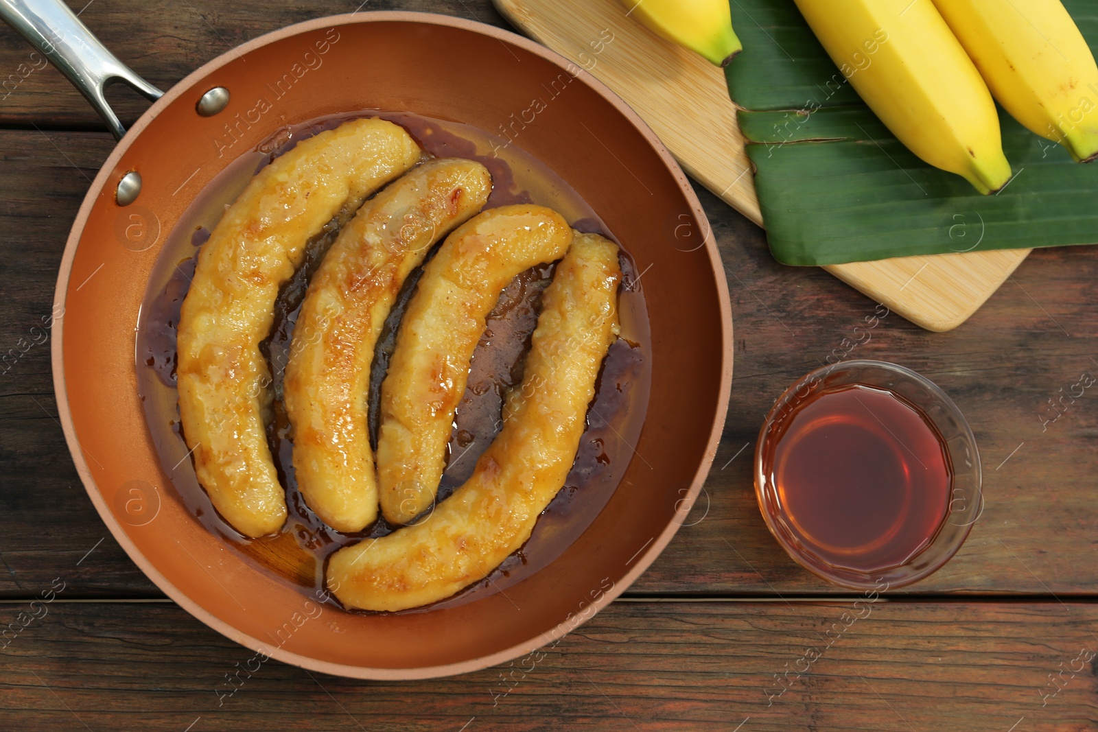 Photo of Delicious fresh and fried bananas with rum on wooden table, flat lay