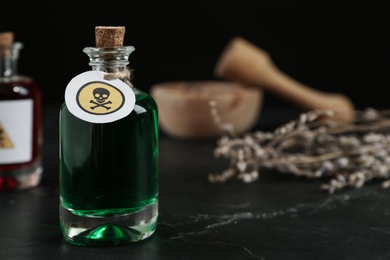 Photo of Glass bottle of poison with warning sign on black table. Space for text