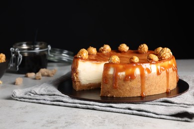 Photo of Sliced delicious cheesecake with caramel and popcorn on light grey table, space for text