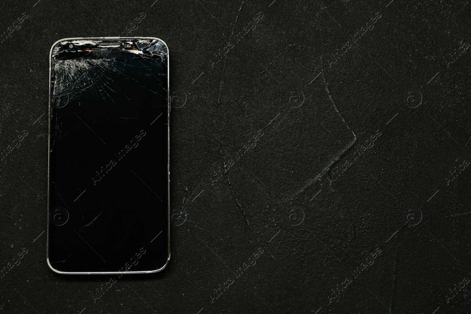 Photo of Damaged smartphone on black table, top view with space for text. Device repairing