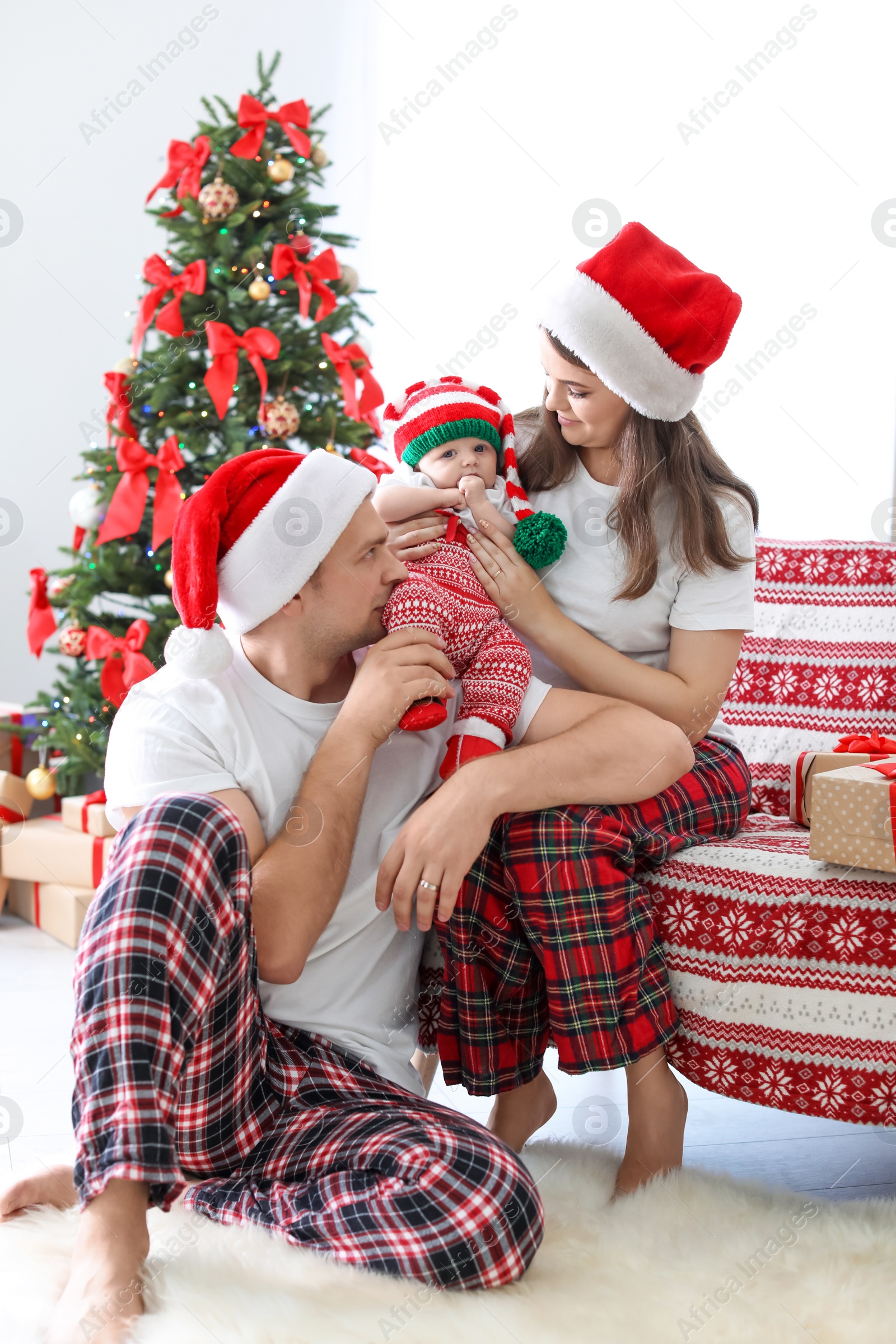 Photo of Happy couple with baby in Christmas hats at home