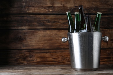 Metal bucket with bottles of beer and ice cubes on wooden table, space for text
