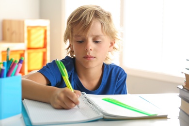 Photo of Little boy doing homework at table indoors