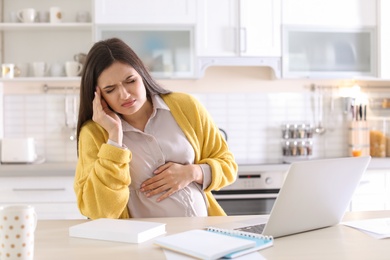 Photo of Young pregnant woman suffering from headache in home office