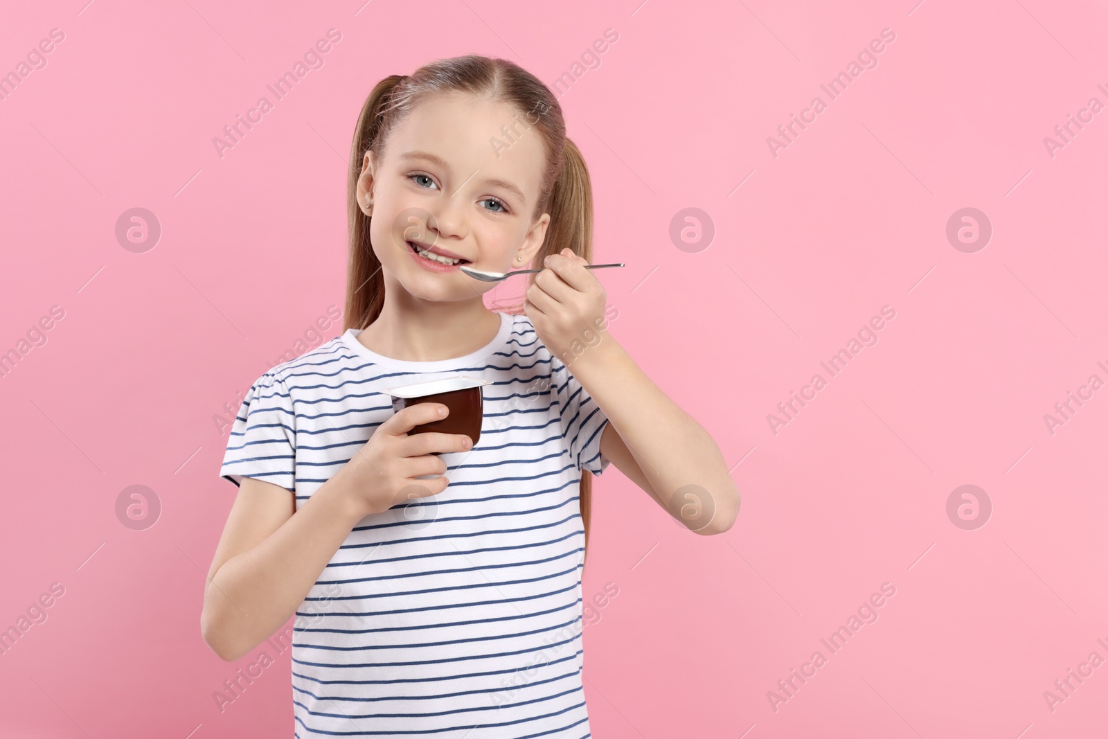 Photo of Cute little girl with tasty yogurt on pink background, space for text