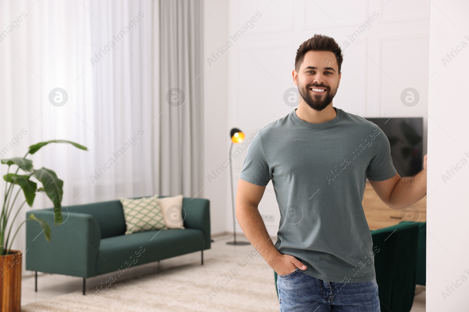 Photo of Happy man standing near white wall at home, space for text. Invitation to come in room