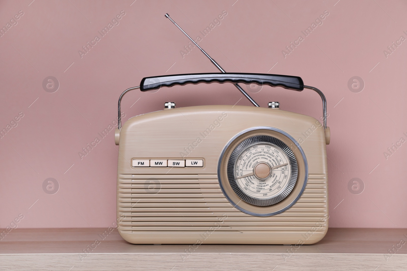 Photo of Retro radio receiver on wooden table against pink background