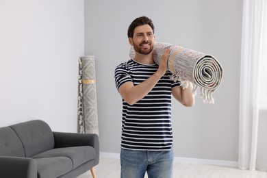 Smiling man holding rolled carpet in room