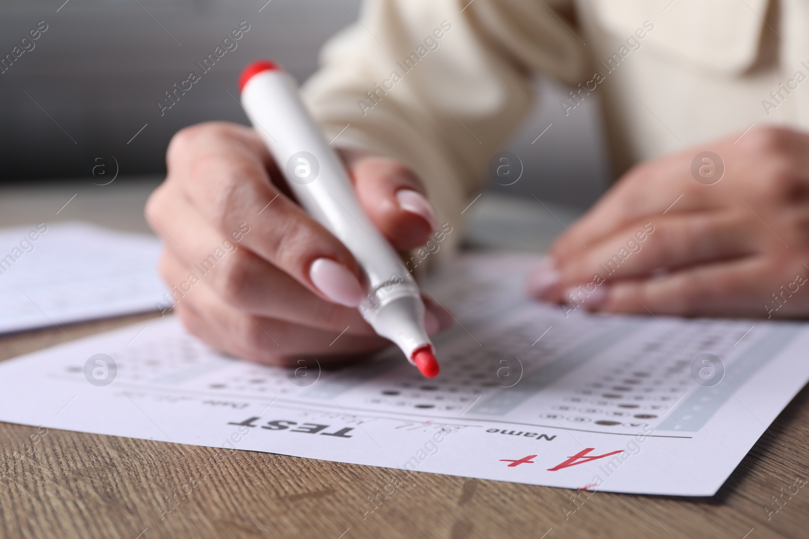Photo of School grade. Teacher writing letter A with plus symbol on answer sheet at wooden table, closeup