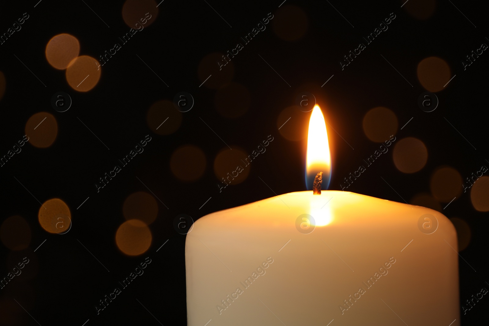 Photo of Burning candle on black background with blurred lights, space for text