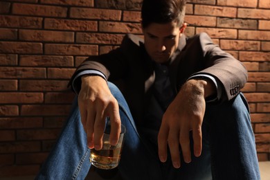 Photo of Addicted man near red brick wall, focus on glass of alcoholic drink
