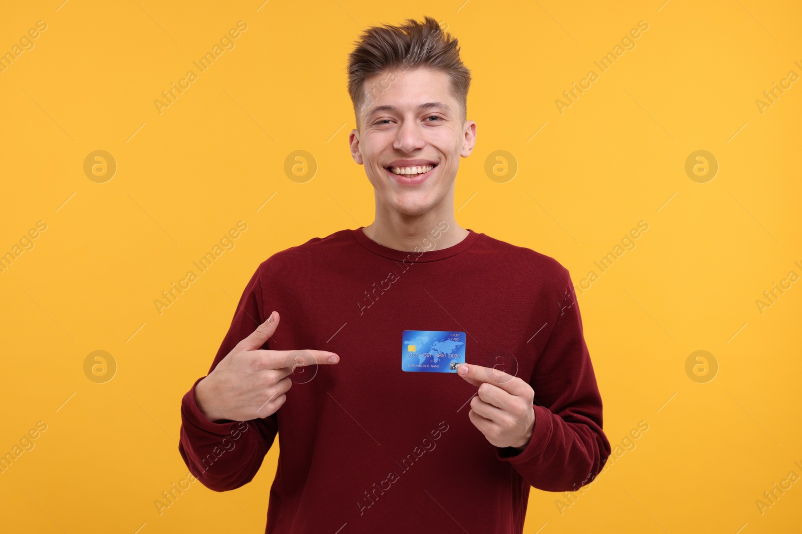 Photo of Happy man pointing at credit card on yellow background