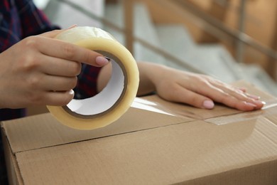 Photo of Woman taping cardboard box indoors, closeup view