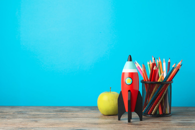 Photo of Bright toy rocket and school supplies on wooden desk. Space for text