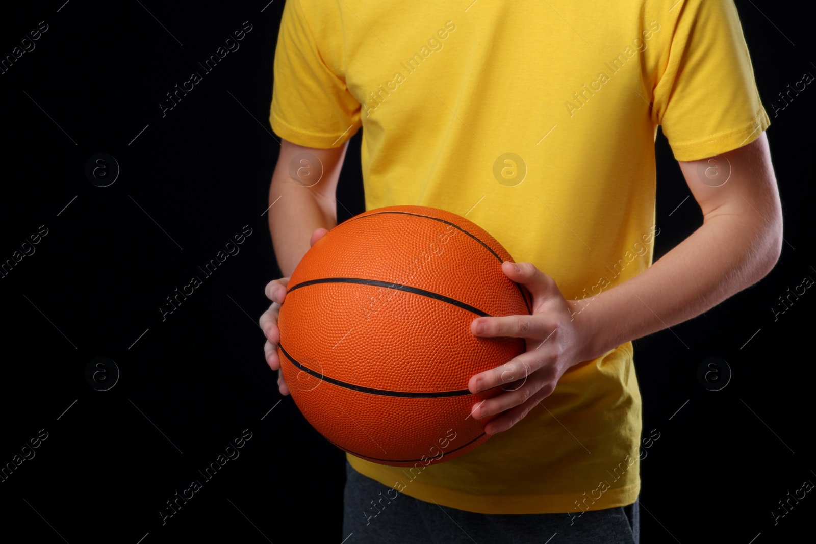 Photo of Boy with basketball ball on black background, closeup. Space for text