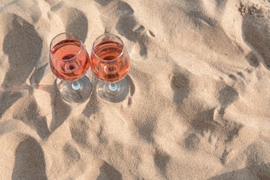 Photo of Glasses of tasty rose wine on sand, above view. Space for text