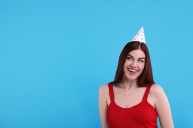 Photo of Happy woman in party hat on light blue background, space for text