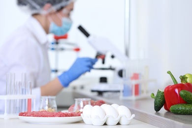 Photo of Different food on table and scientist proceeding quality control in laboratory