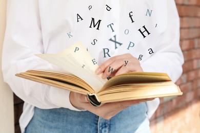 Woman reading book with letters flying over it outdoors, closeup