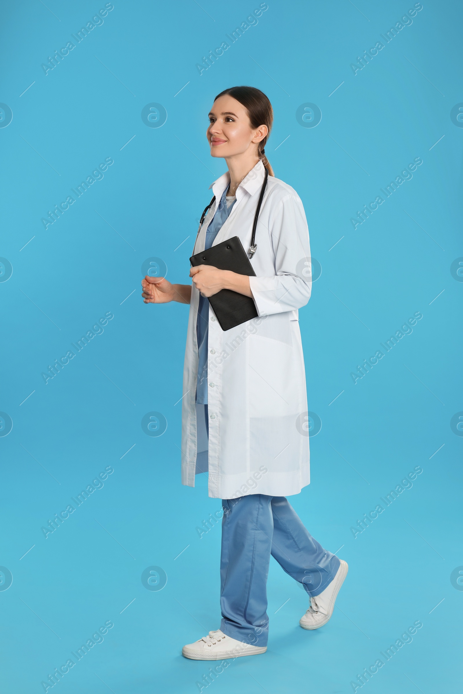 Photo of Doctor with clipboard and stethoscope walking on blue background