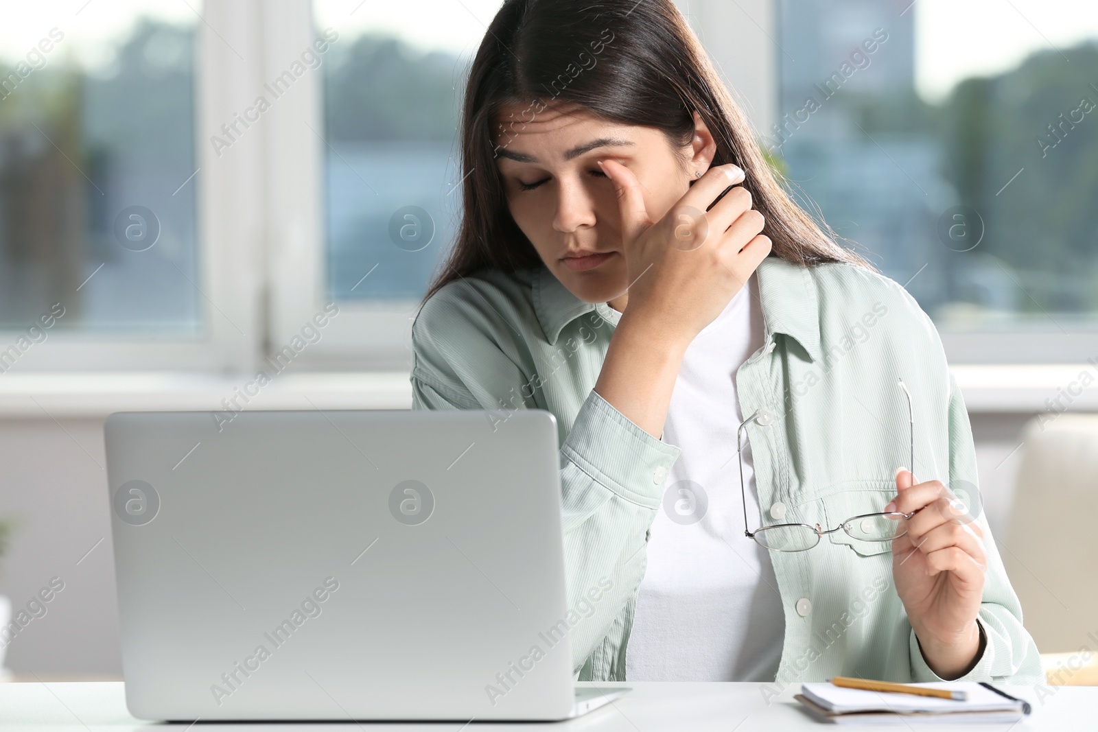 Photo of Young woman suffering from eyestrain at desk in office