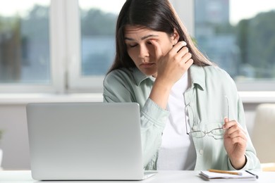 Young woman suffering from eyestrain at desk in office