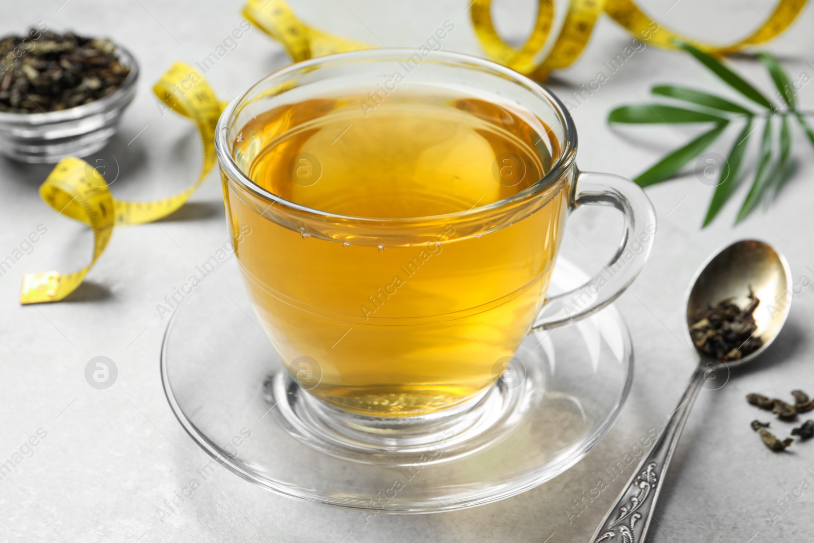 Photo of Cup of herbal diet tea and measuring tape on white table, closeup. Weight loss concept