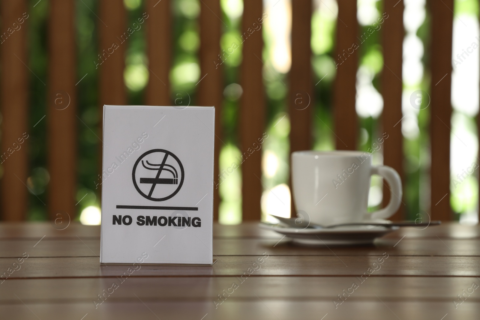 Photo of No Smoking sign and cup of drink on wooden table against blurred background, selective focus