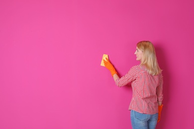 Woman in gloves cleaning color wall with rag