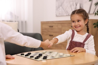 Photo of Happy girl shaking hands with her brother after playing checkers at home