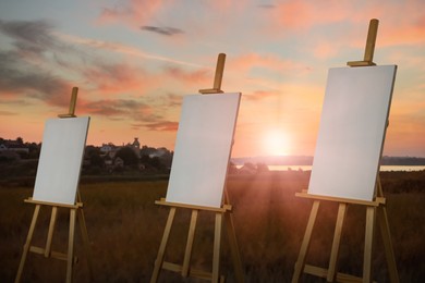 Wooden easels with blank canvases in field at sunset 