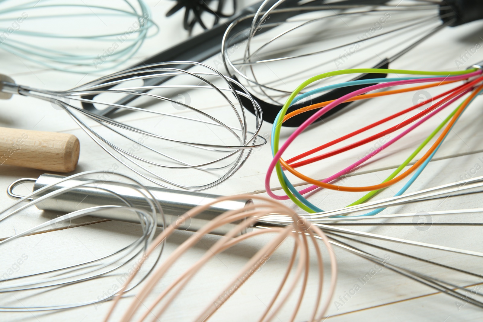 Photo of Different whisks on white wooden table, closeup