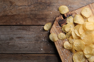 Photo of Board with delicious crispy potato chips on wooden table, top view. Space for text