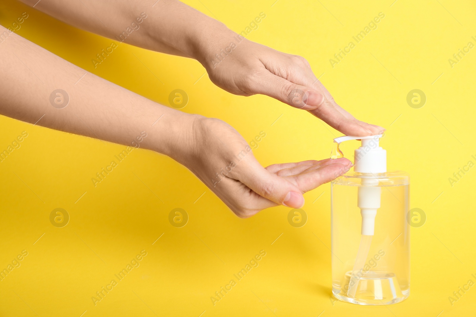 Photo of Woman applying antiseptic gel on hand against yellow background, closeup