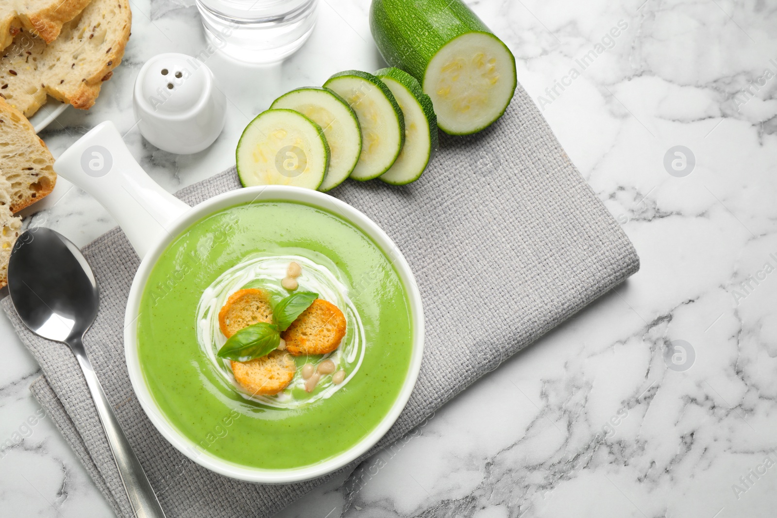 Photo of Tasty homemade zucchini cream soup served on marble table, flat lay
