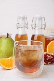 Tasty kombucha with ice cubes and fresh fruits on white tiled table, closeup