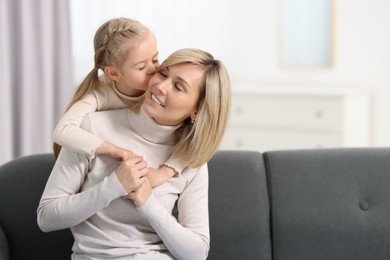 Photo of Daughter kissing her happy mother on sofa at home. Space for text