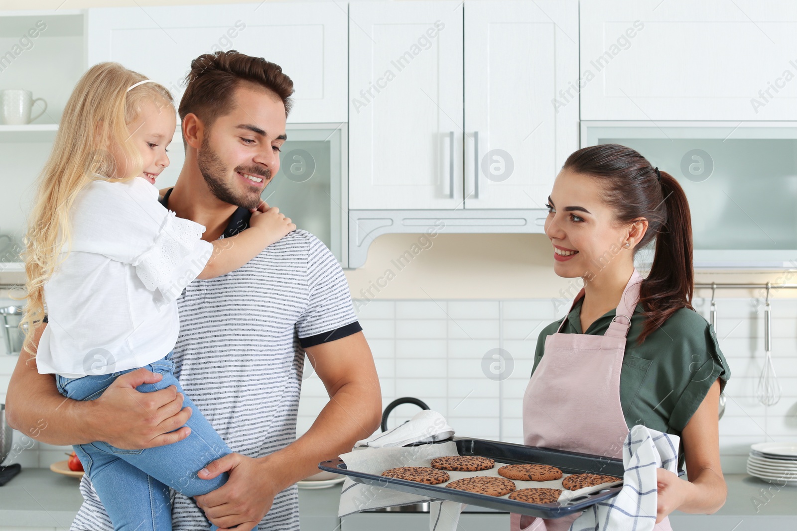 Photo of Young woman treating her family with homemade oven baked cookies in kitchen