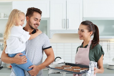 Photo of Young woman treating her family with homemade oven baked cookies in kitchen