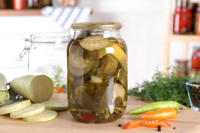 Photo of Jar with pickled zucchinis on wooden board indoors