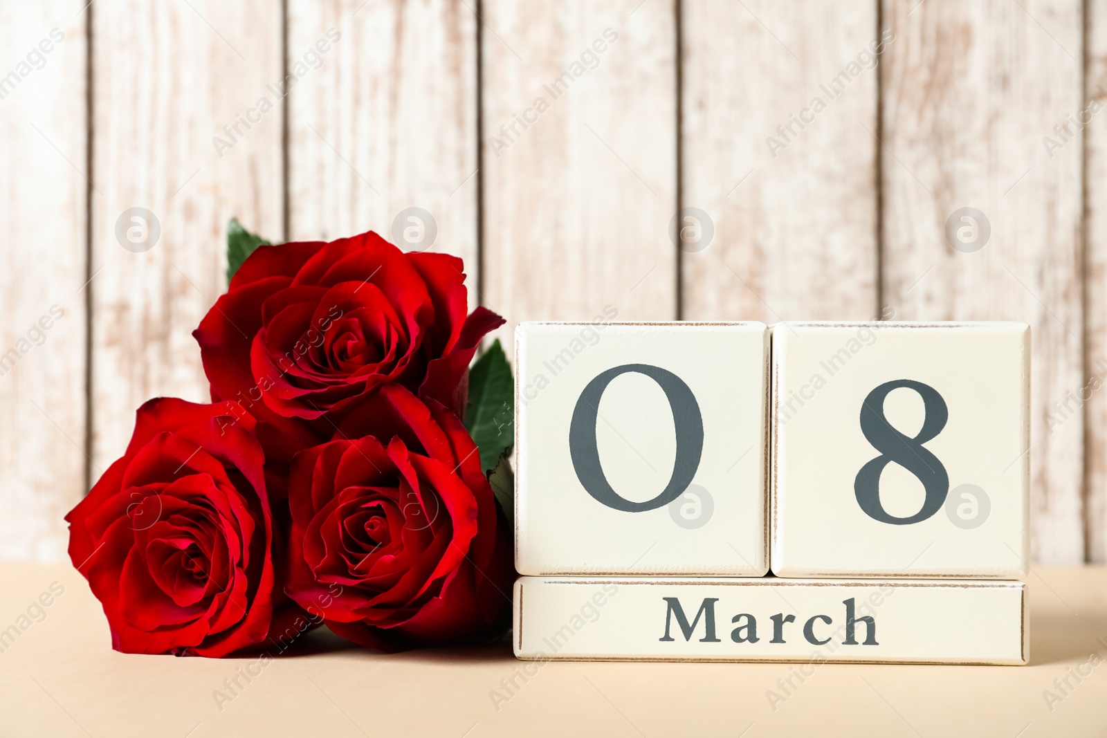 Photo of Wooden block calendar with date 8th of March and roses on table against light background, space for text. International Women's Day