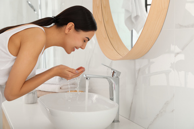 Photo of Young woman washing face with cosmetic product in bathroom