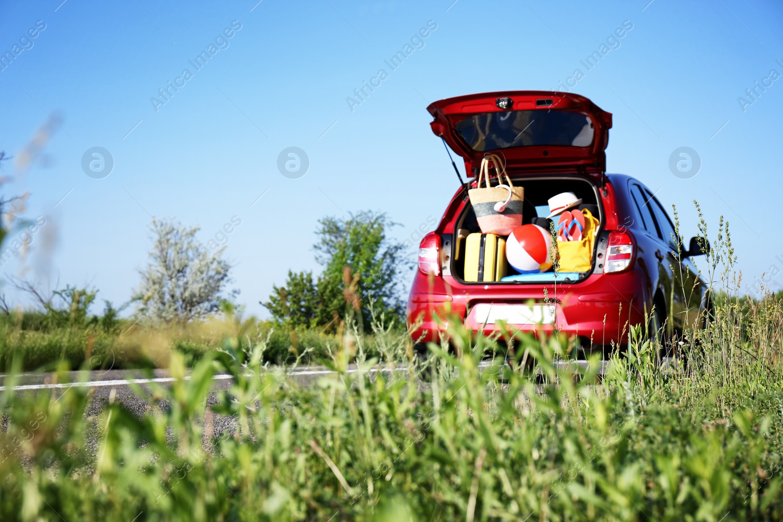 Photo of Family car with open trunk full of luggage on highway. Space for text