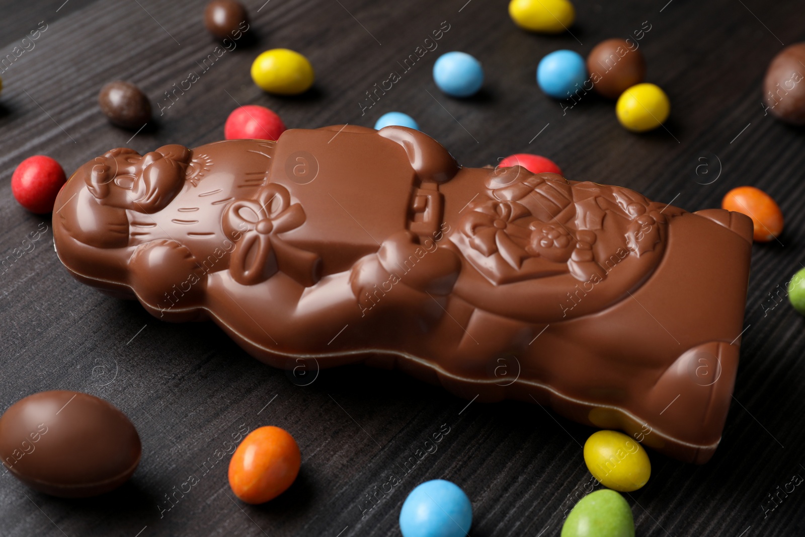 Photo of Composition of chocolate Santa Claus among sweets on dark grey wooden table, closeup