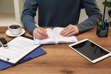 Photo of Man taking notes at wooden table indoors, closeup