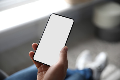 Man holding mobile phone with empty screen indoors, closeup