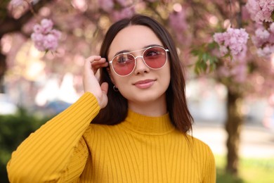 Beautiful woman in sunglasses near blossoming tree on spring day