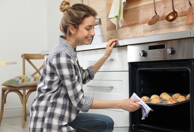 Photo of Young woman baking cookies in oven at home